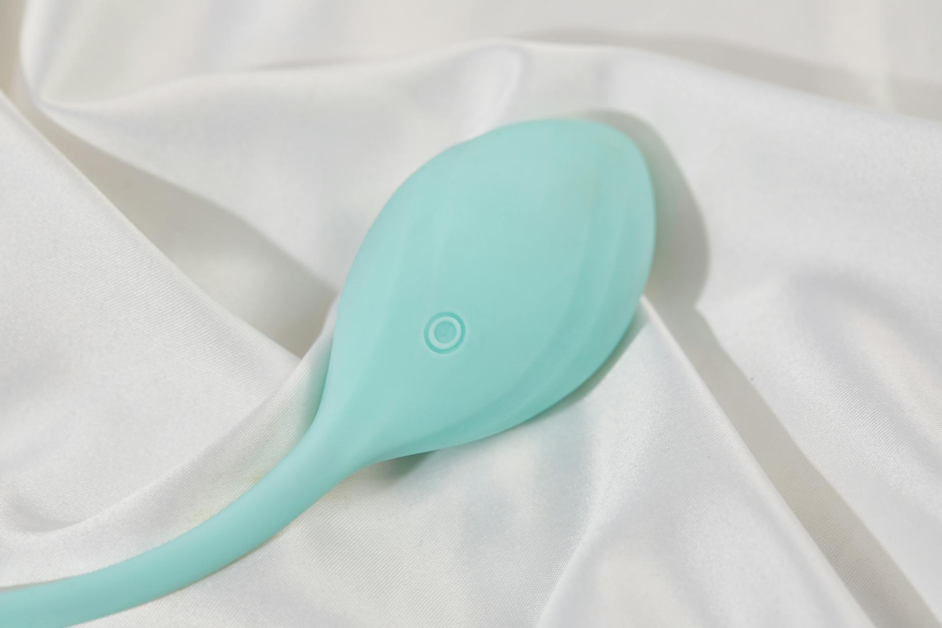 Stylish teal vibrator on smooth white silk fabric
