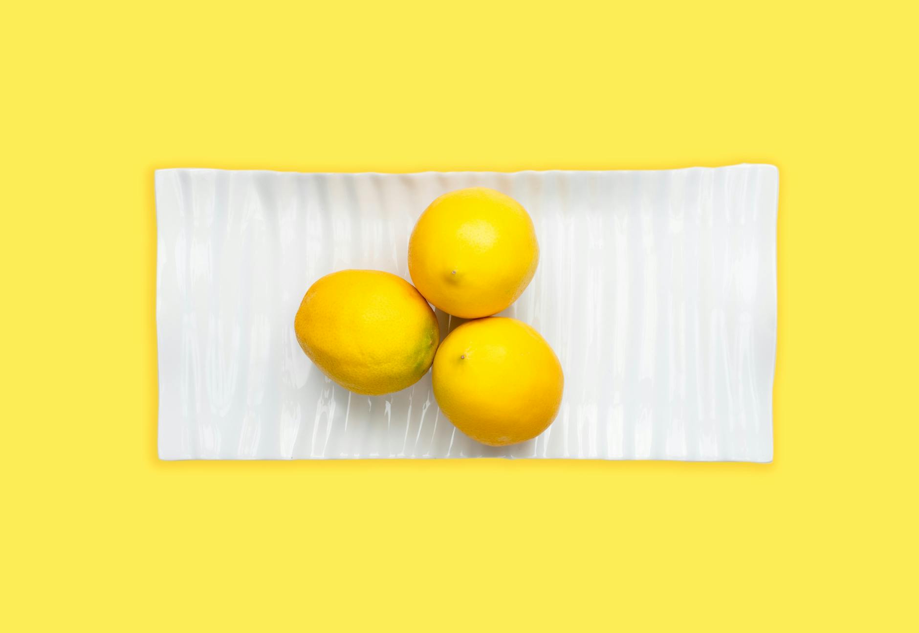 Fresh lemons arranged on white plate against vibrant yellow background, symbolizing renewal and sensation