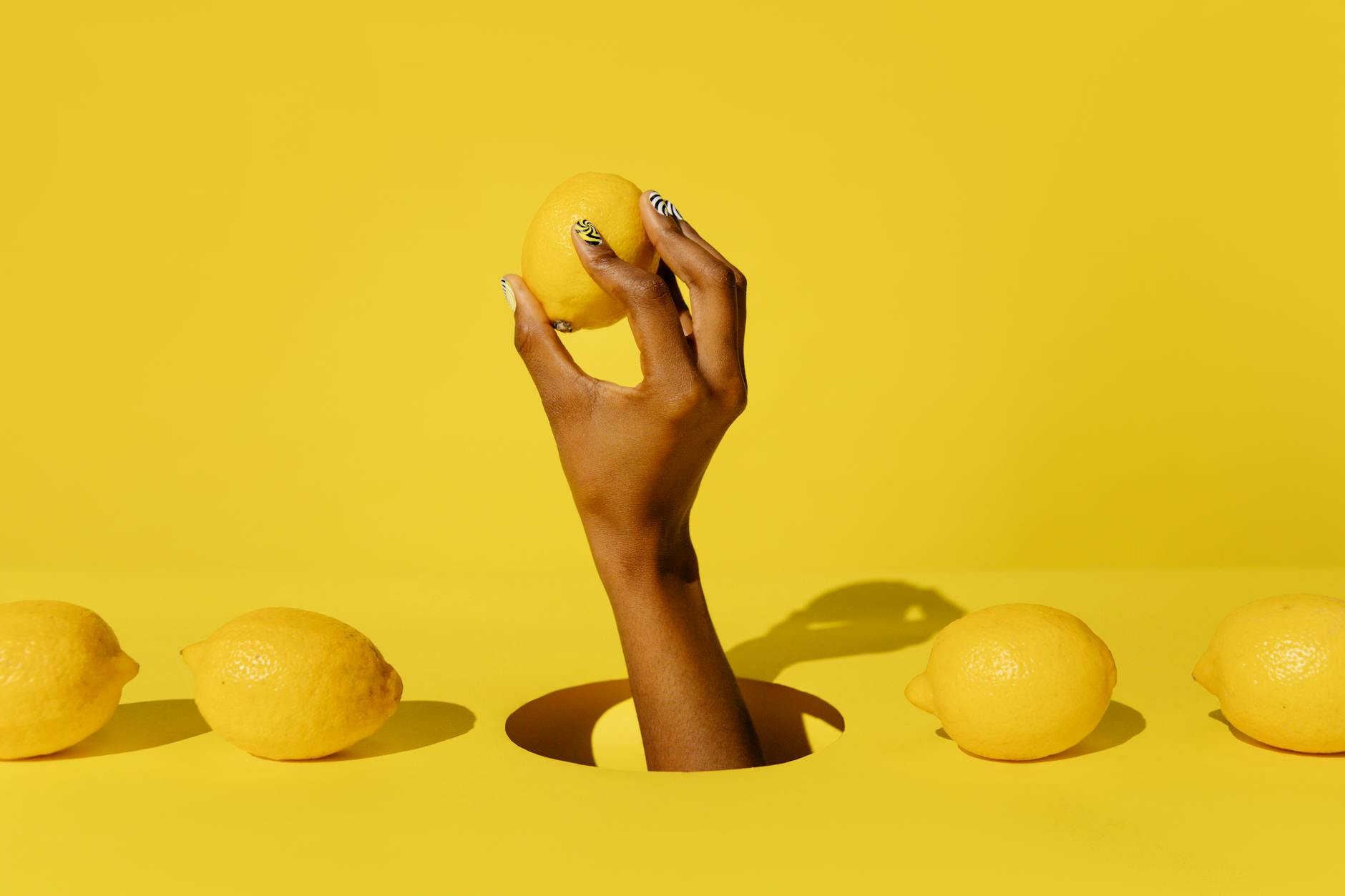 A creative composition featuring a hand holding a lemon against a vivid yellow background, conveying freshness and citrusy appeal