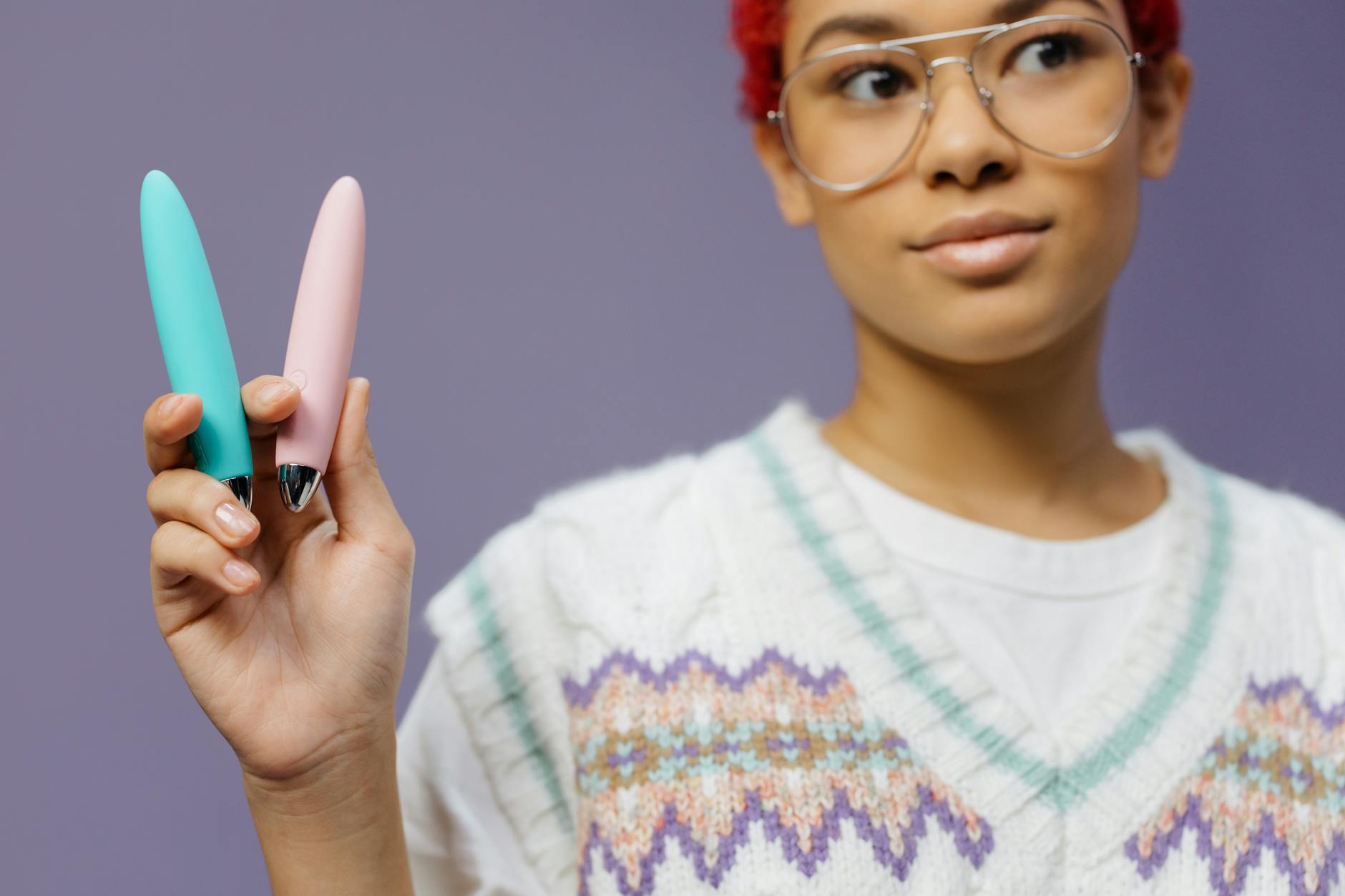 Person holding colorful vibrators against a purple background, representing different pleasure tools and sensation options
