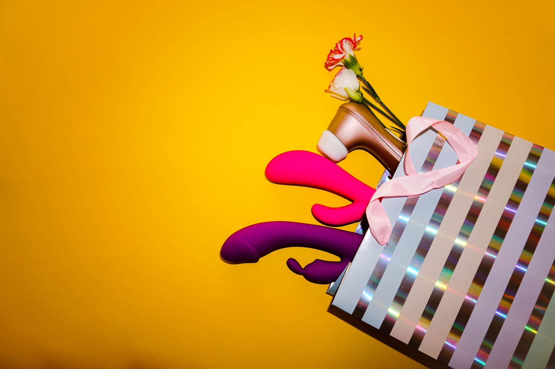 Colorful lemon vibrators with fresh flowers in a gift bag against a bright yellow background